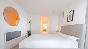 Une chambre à coucher moderne avec un grand lit, un miroir rond, une lampe de chevet et un tableau encadré accroché au mur.