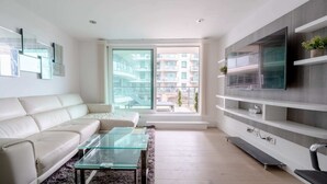 Un salon moderne avec un canapé blanc, une table basse en verre et un grand téléviseur à écran plat fixé sur un mur gris.