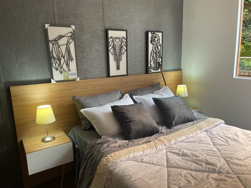 A bedroom with a wooden headboard, a bed with multiple pillows, bedside lamps, and three framed artworks on the wall.