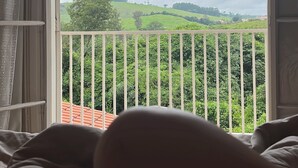 Un dormitorio con vista a un paisaje verde a través de la barandilla del balcón.