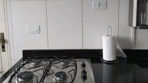 Una cocina con estufa a gas, dispensador de toallas de papel y un guante de horno rojo en la pared.