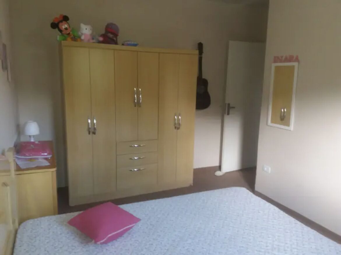 Um quarto com cama, guarda-roupa, um violão e um espelho.