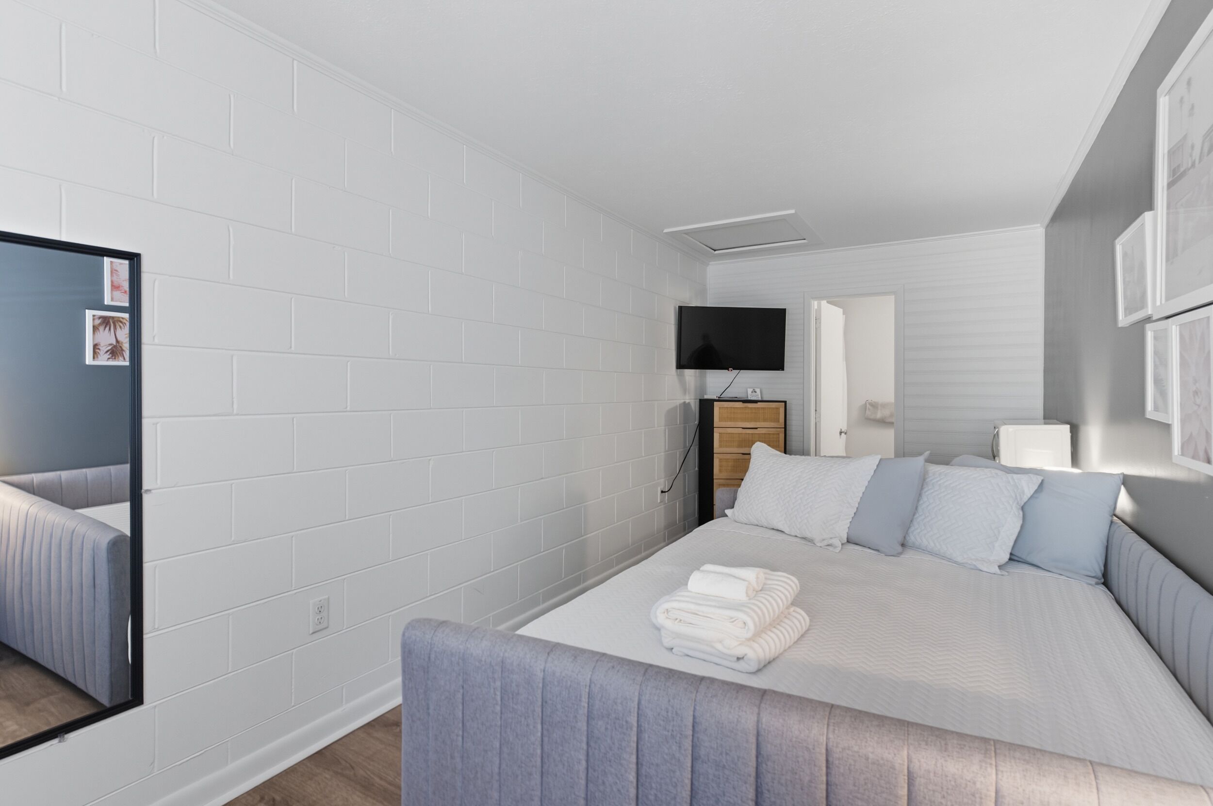 Moderni hotellihuone, jossa on suuri sänky, taulutelevisio, peili ja puinen yöpöytä.