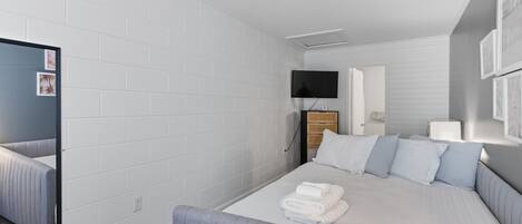 Moderni hotellihuone, jossa on suuri sänky, taulutelevisio, peili ja puinen yöpöytä.