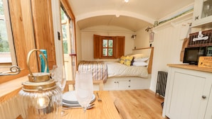 A cozy room with a wooden table set for dining, a bed with patterned bedding, and a window with curtains. - The Happy Hut (Christchurch)