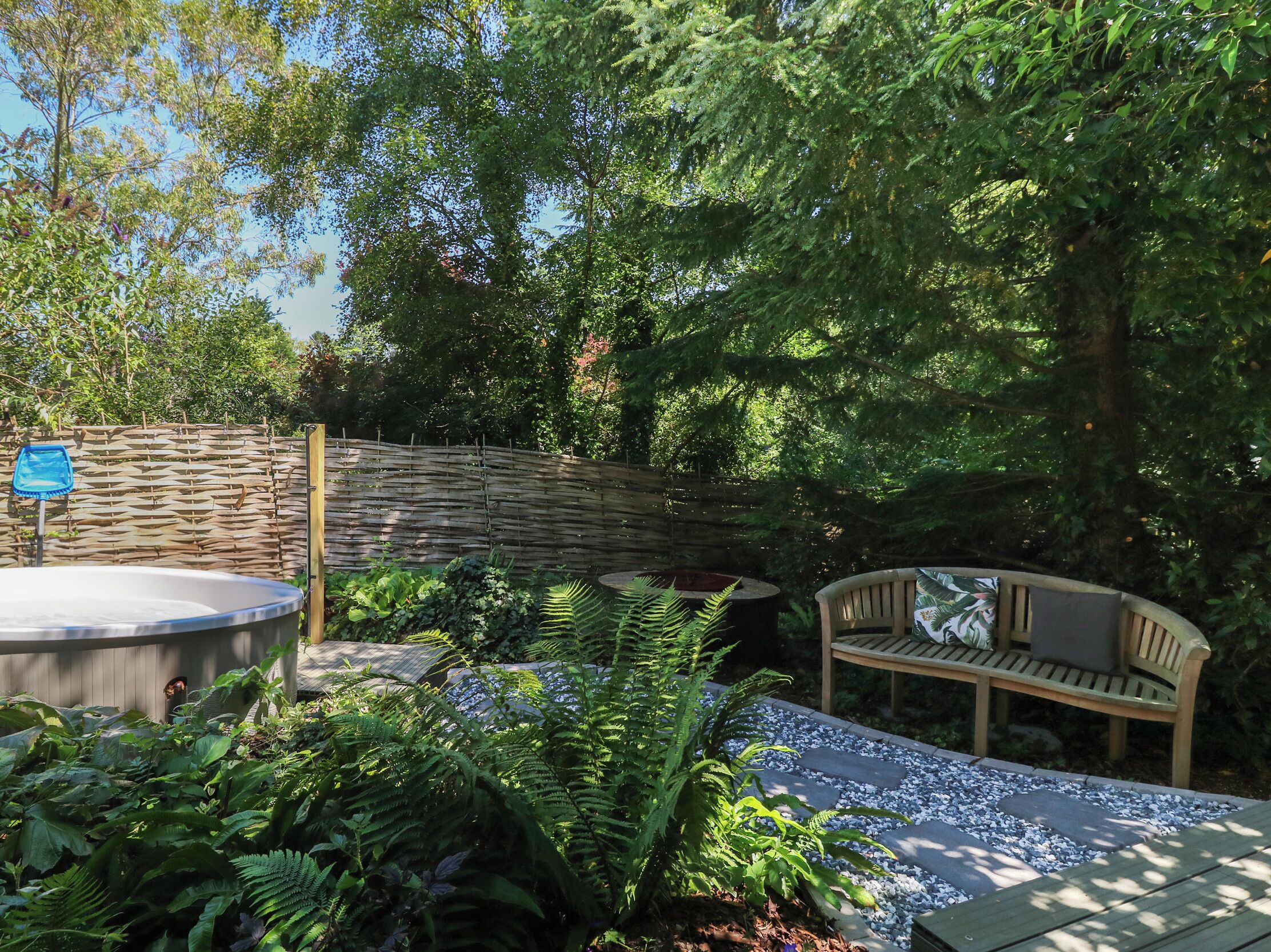 A garden area with a hot tub, a wooden bench, and a stone wall.