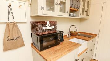 A kitchen with white cabinets, a wooden countertop, a microwave, a coffee maker, and a hanging bag.