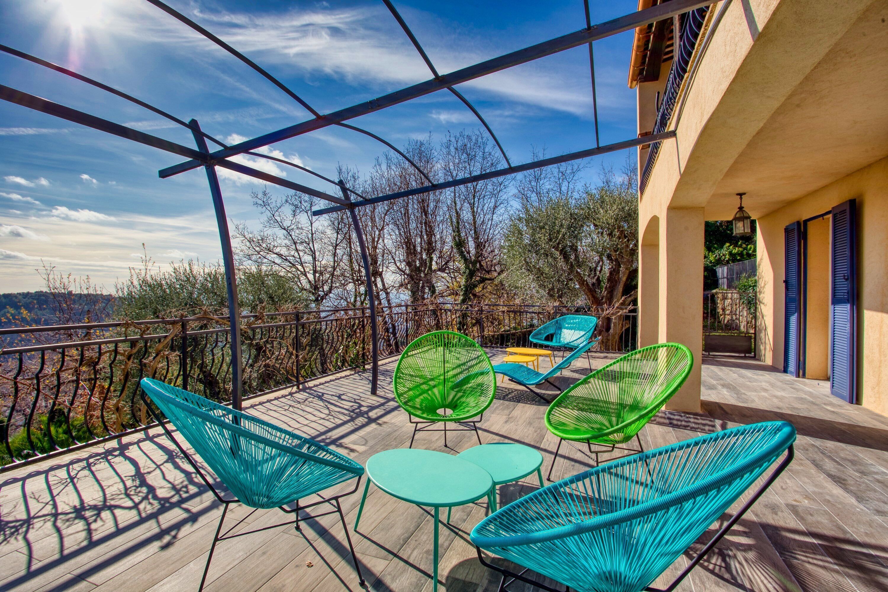 Una terraza con sillones y mesas de mimbre, con vistas a un paisaje pintoresco.