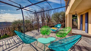 Una terraza con sillones y mesas de mimbre, con vistas a un paisaje pintoresco.