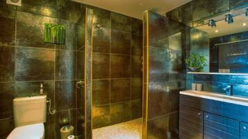 Un baño moderno con azulejos oscuros, cabina de ducha de cristal, inodoro y tocador con espejo.