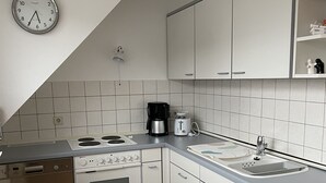 Moderni keittiö, jossa on valkoiset kaapit, sisäänrakennettu uuni, astianpesukone, kahvinkeitin ja seinällä oleva kello.