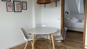 Moderni huone, jossa on pyöreä pöytä, kaksi tuolia, riippuvalaisin ja taustalla sänky.