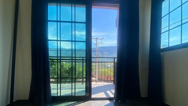 A room with a large sliding glass door leading to a balcony with a view of greenery and mountains. - Casa Camotlan (La Yesca)