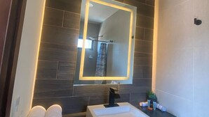 A modern bathroom with a white sink, dark tiles, a mirror with illuminated frame, and towels on the counter. - Casa Camotlan (La Yesca)