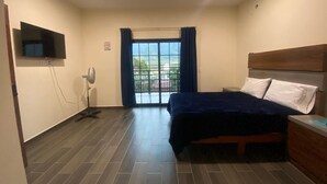 A bedroom with a bed, a TV mounted on the wall, a fan, and a window with curtains. - Casa Camotlan (La Yesca)