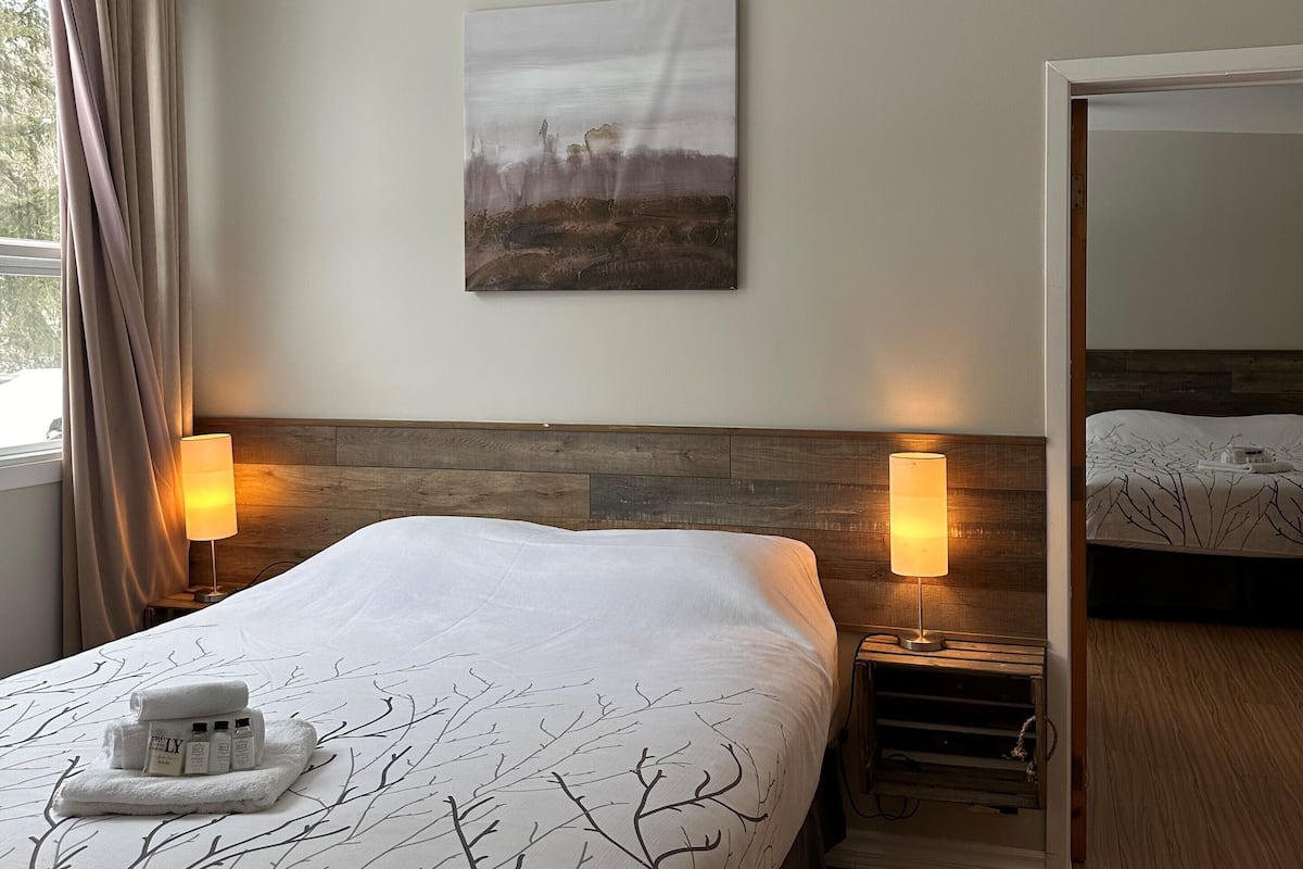Ein Hotelzimmer mit einem großen Bett, zwei Nachttischlampen, einem Kopfteil, einem Gemälde an der Wand und einem Spiegel an der Tür.