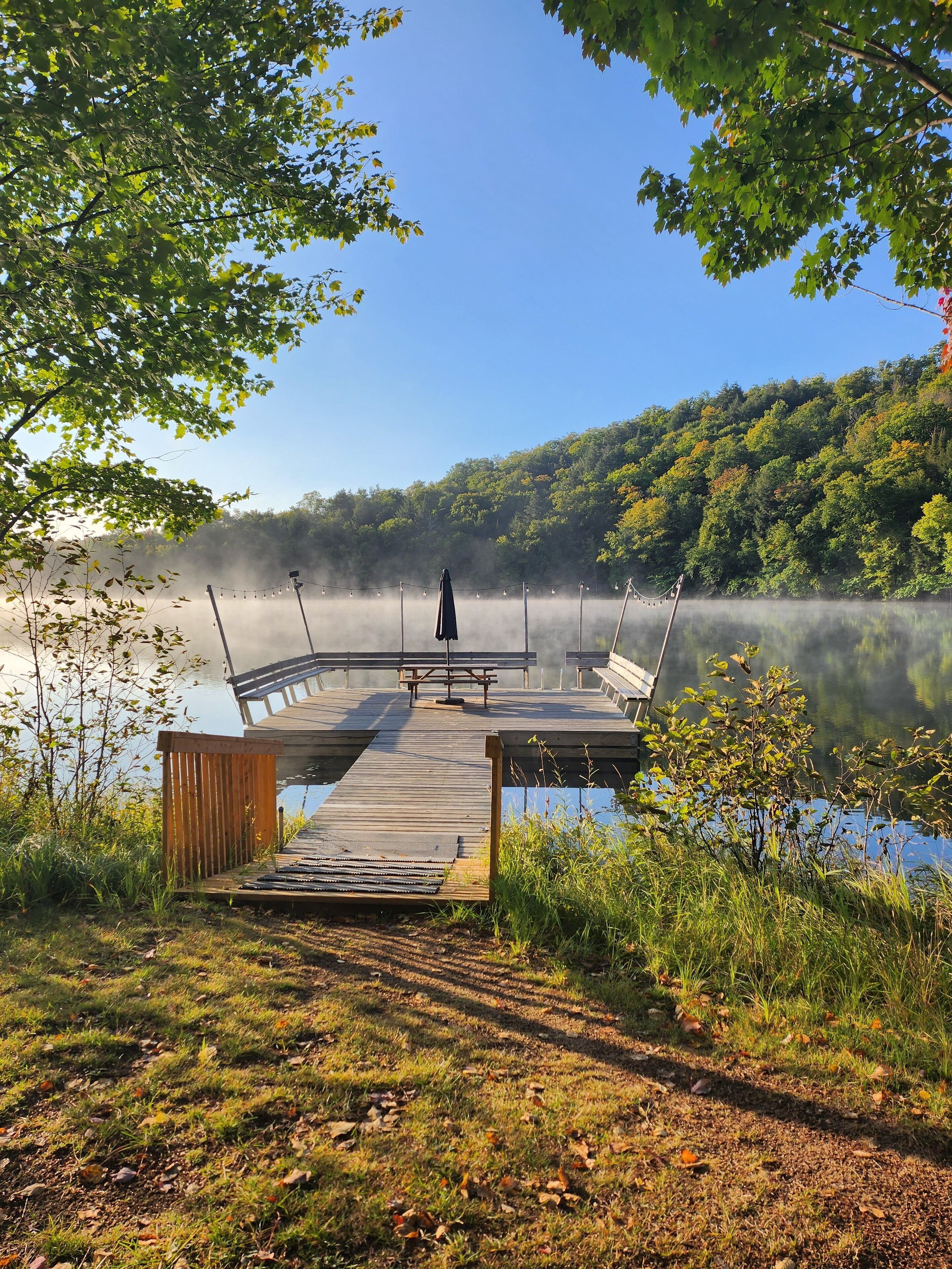 A wooden dock extending into a calm lake with a forested hillside in the background.
