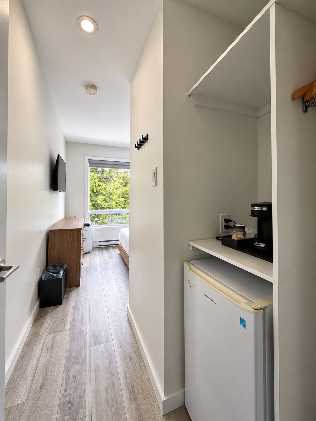 Cocina compacta con refrigerador, cafetera y ventana con vista a follaje.