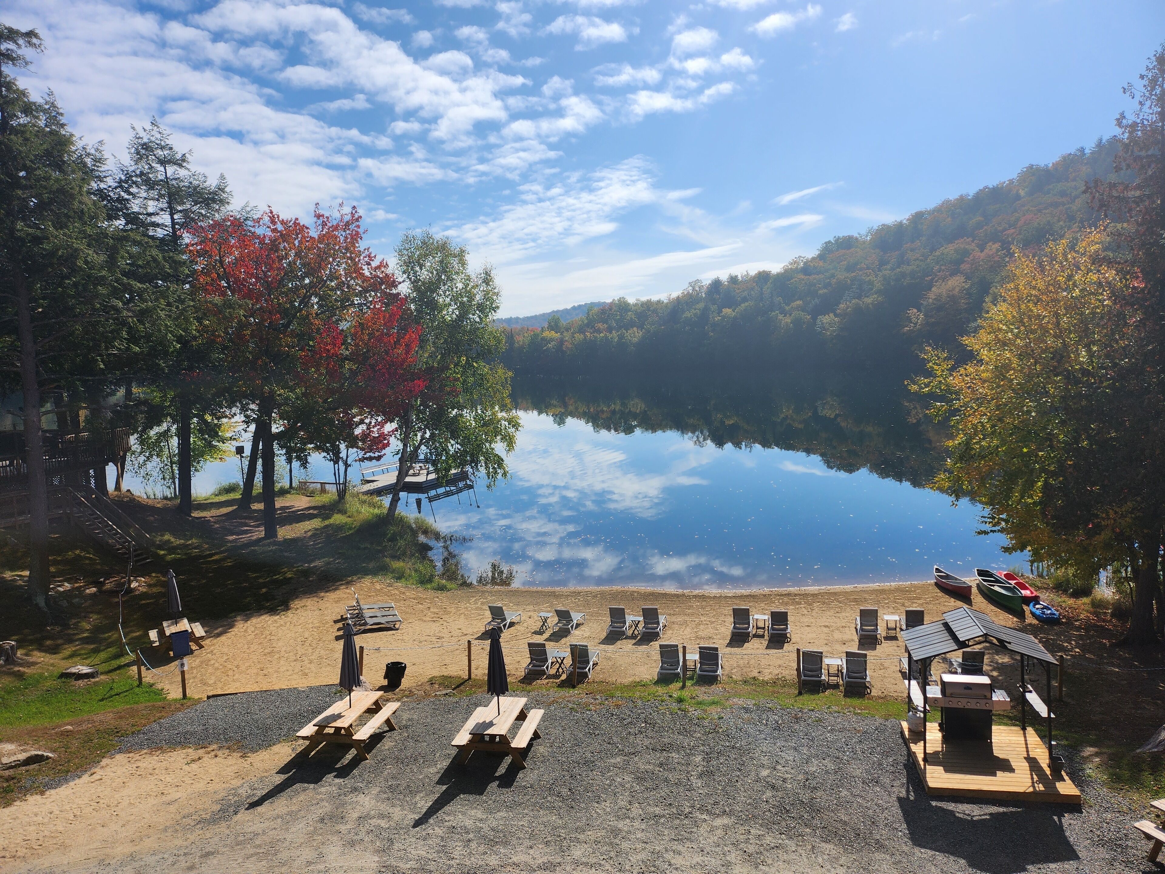 Vista su un lago con un pontile, tavoli da picnic e sedie a sdraio.