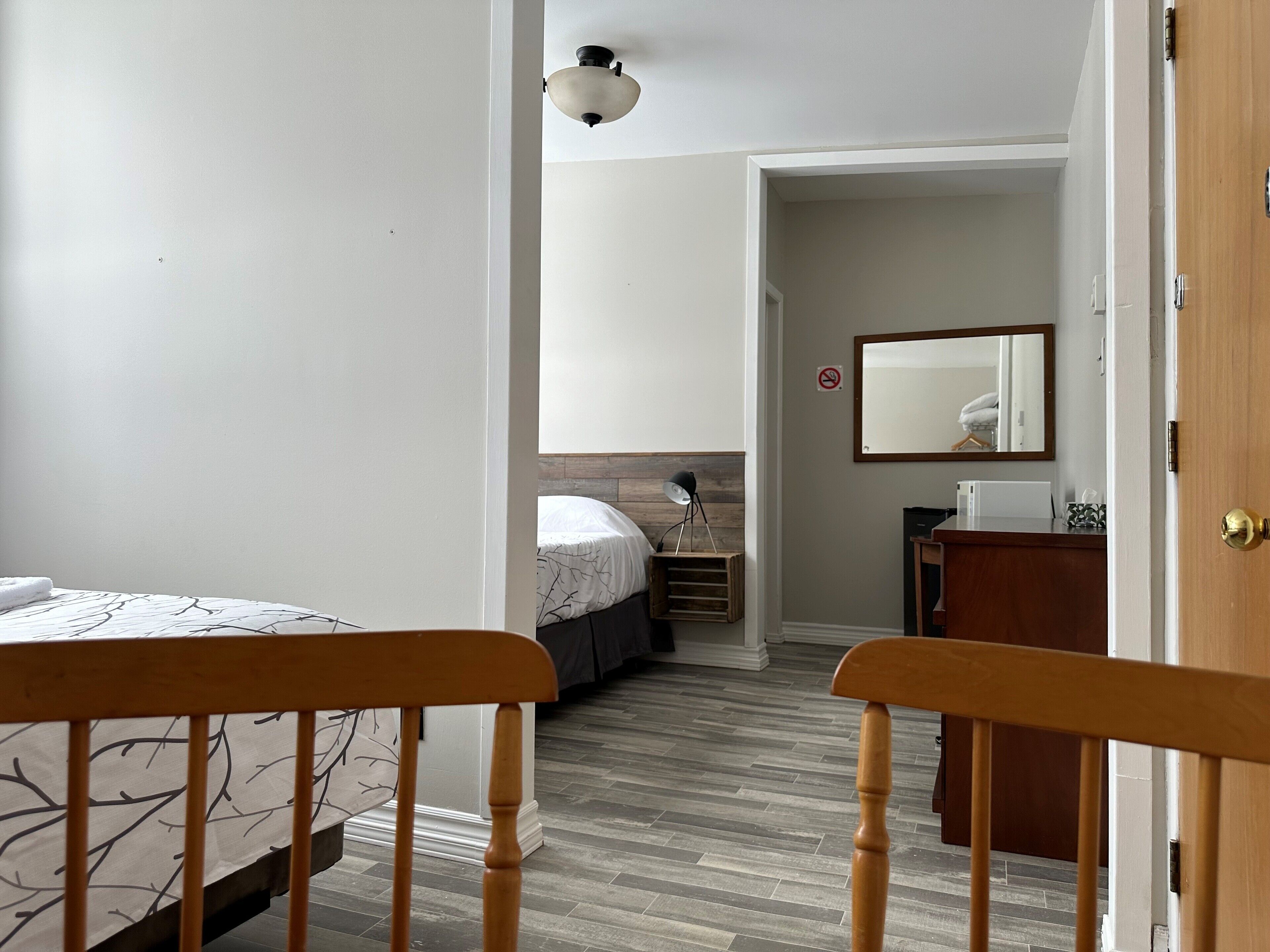 Un dormitorio con cama, mesita de noche, cómoda, espejo y puerta que da a otra habitación.