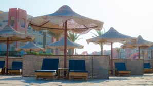 A beach area with lounge chairs and thatched umbrellas, set against a backdrop of buildings. - Oyster Bay Beach Suites (Marsa Alam)