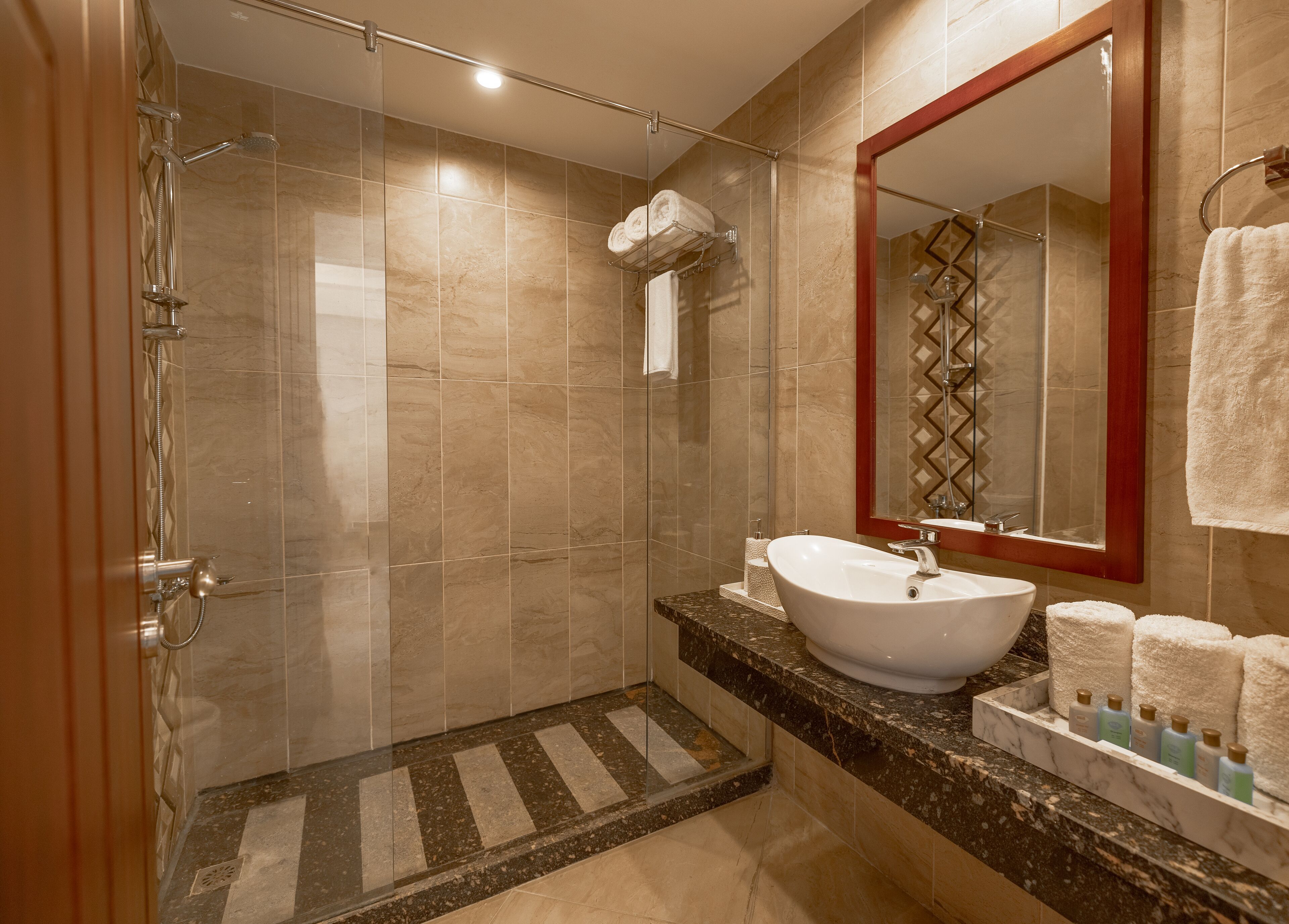 Un baño moderno con ducha de vidrio, encimera de mármol, lavabo blanco y espejo con marco decorativo.