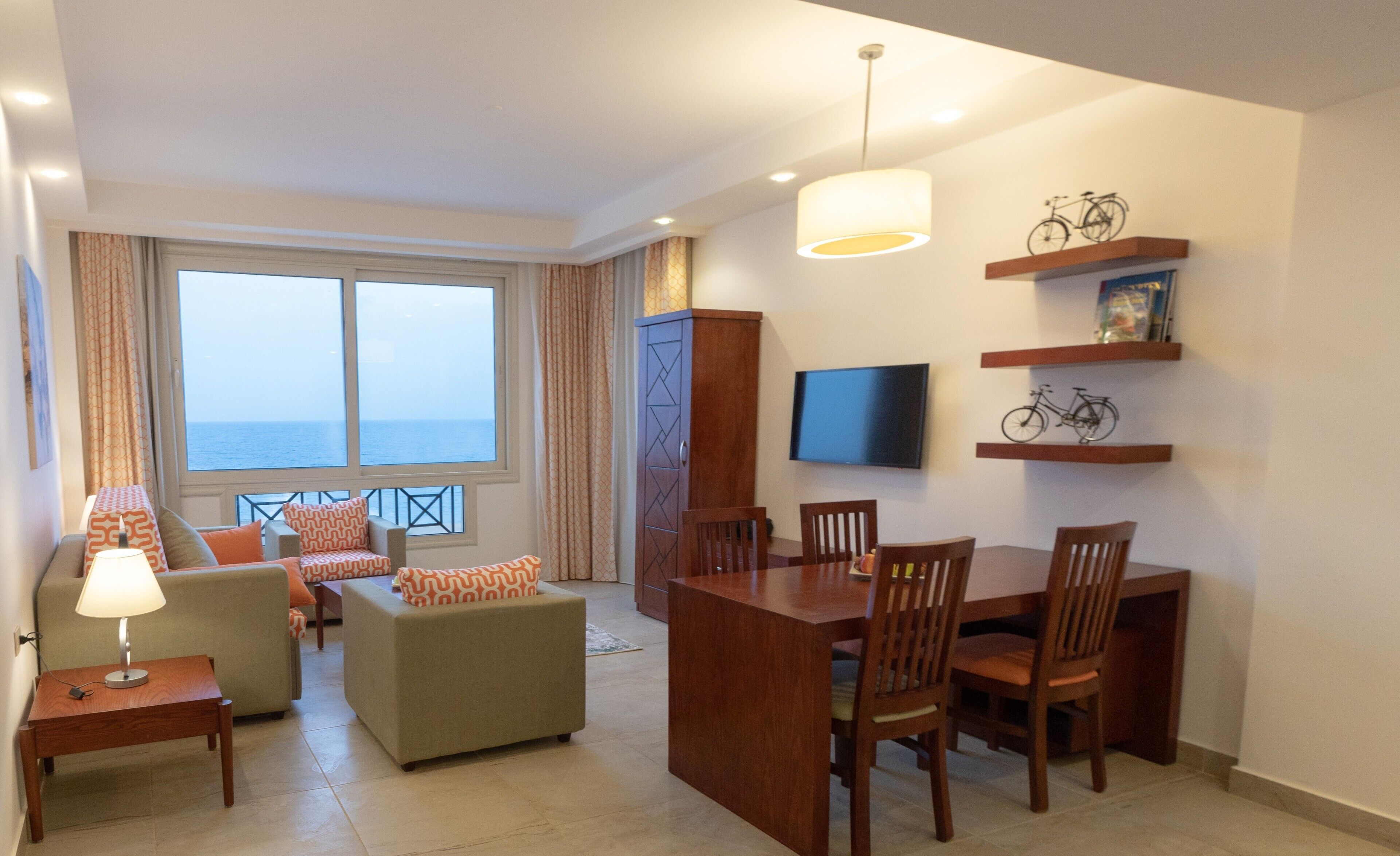 Una sala de estar moderna con comedor, ventanas amplias, televisor y vista al mar.