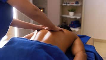 Uma pessoa recebendo uma massagem nas costas em um quarto com uma toalha azul e prateleiras ao fundo.