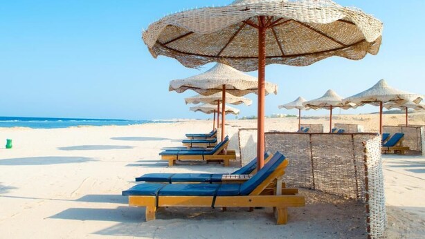 A beach with rows of sun loungers and woven umbrellas. - Oyster Bay Beach Suites (Marsa Alam)