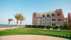 A multi-story hotel with balconies, a landscaped garden, and a view of the beach. - Oyster Bay Beach Suites (Marsa Alam)
