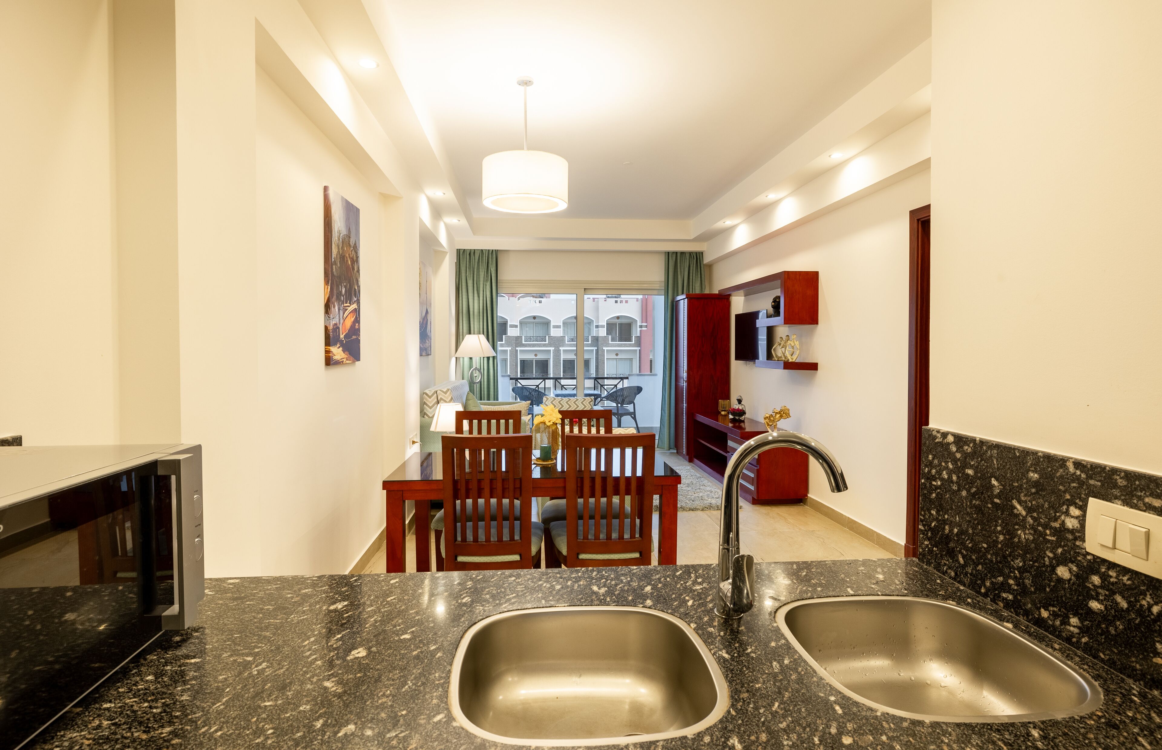 A modern kitchen with granite countertops, stainless steel sinks, and a dining area with wooden chairs and a table.