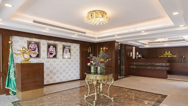A lobby with a reception desk, a decorative table with a vase of flowers, and framed portraits on the wall. - Laten Suites Prince sultan (Jeddah)