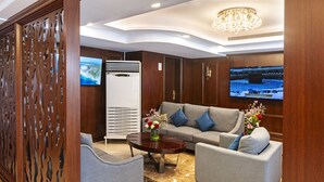 A modern living room with a grey sofa, two armchairs, a coffee table, and a TV mounted on the wall. - Laten Suites Prince sultan (Jeddah)