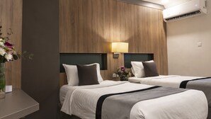 A hotel room with two beds, a nightstand, a lamp, and a vase with flowers. - Laten Suites Prince sultan (Jeddah)