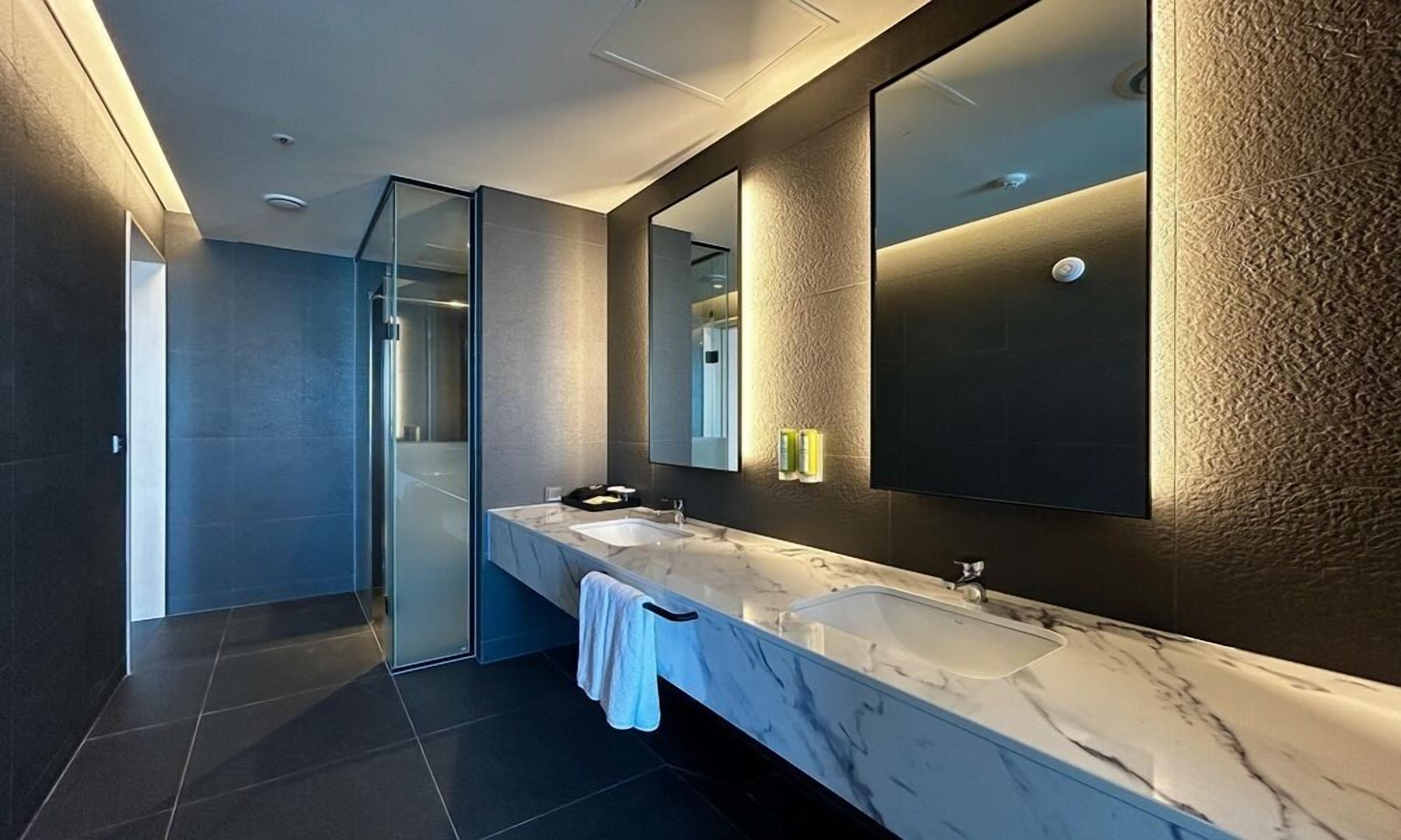 Un baño moderno con un espejo grande, dos lavamanos y una cabina de ducha de vidrio.