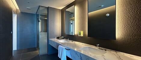 Un baño moderno con un espejo grande, dos lavamanos y una cabina de ducha de vidrio.