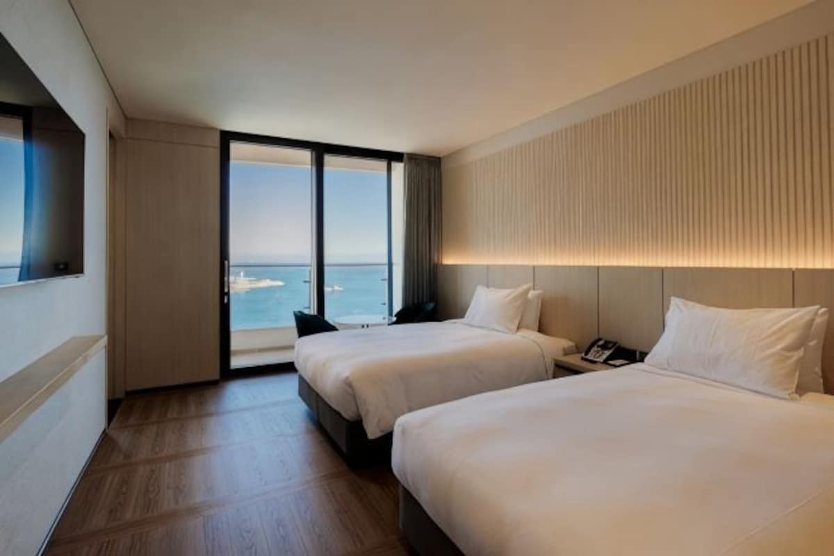 Habitación de hotel con dos camas, un ventanal con vistas al mar y un diseño moderno.