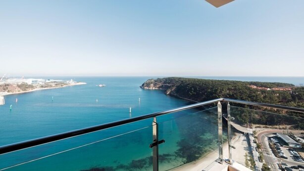 A coastal view from a balcony with a clear view of the sea, a road, and a distant island. - Tanibay Hotel & Wedding (Ulsan)