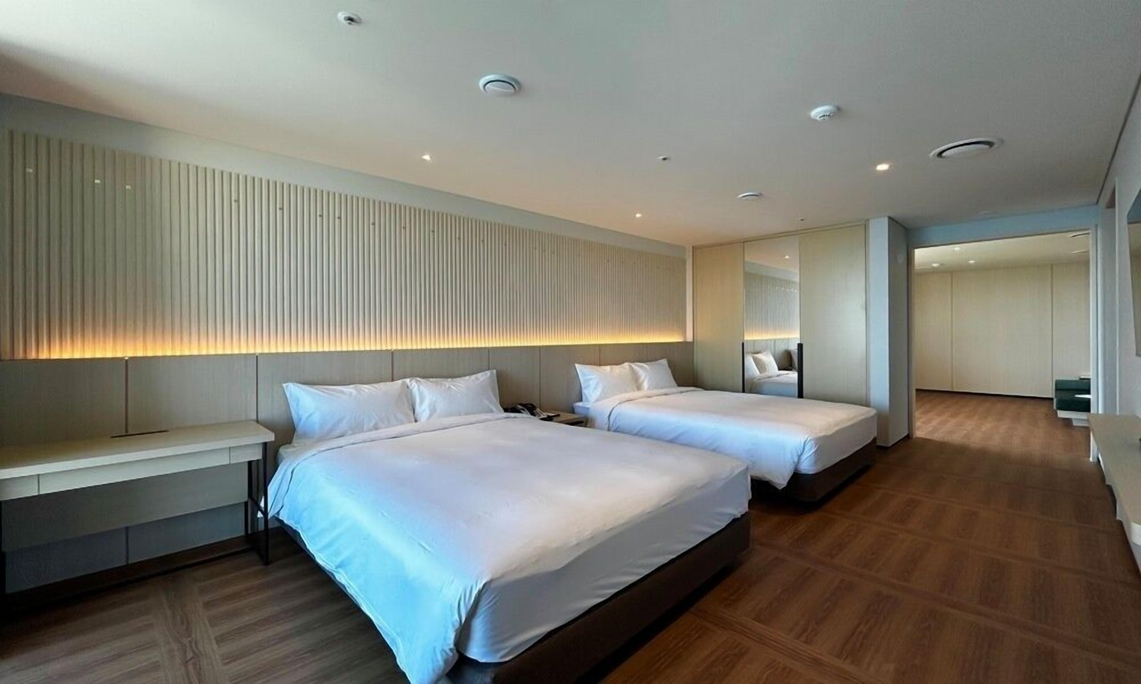 Une chambre d’hôtel moderne avec deux lits, une table de chevet, un grand miroir et un plancher en bois.