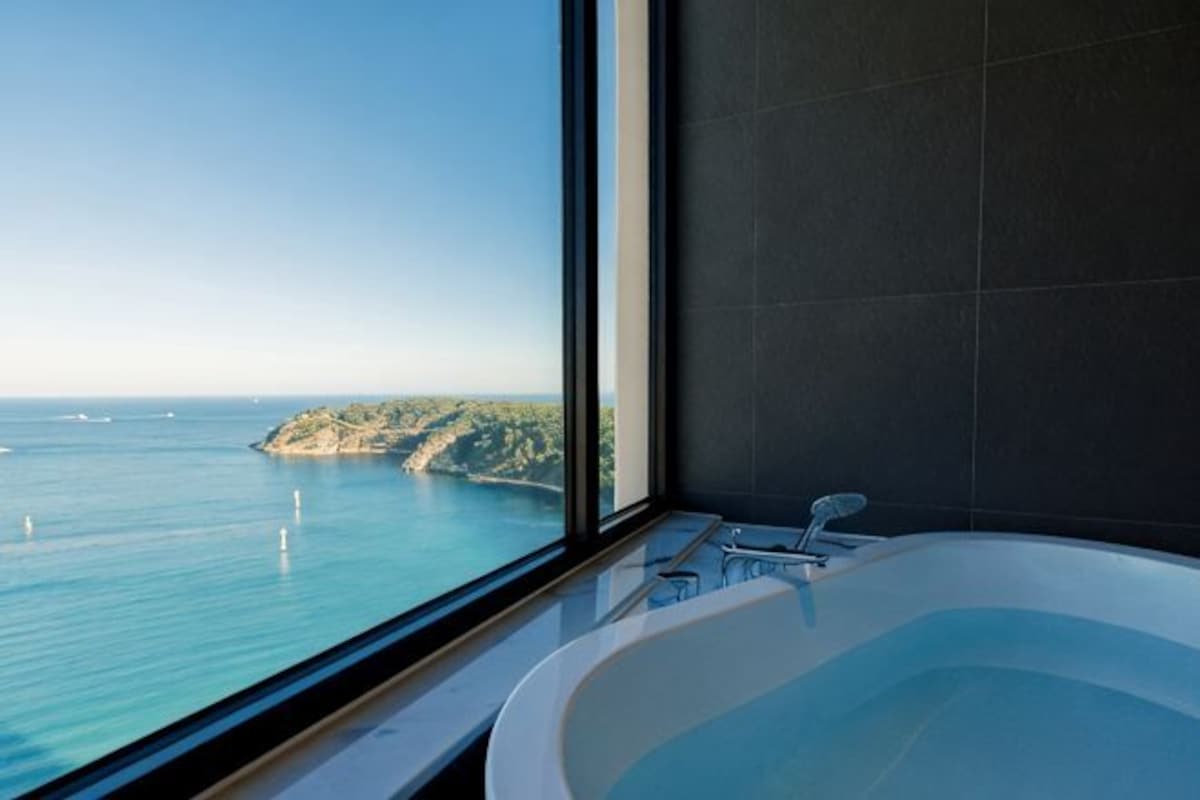 Un baño con una bañera grande, vista al mar y una ventana.