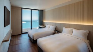 A hotel room with two beds, a large window with a view of the ocean, a bedside table with a phone, and a wall-mounted TV. - Tanibay Hotel & Wedding (Ulsan)