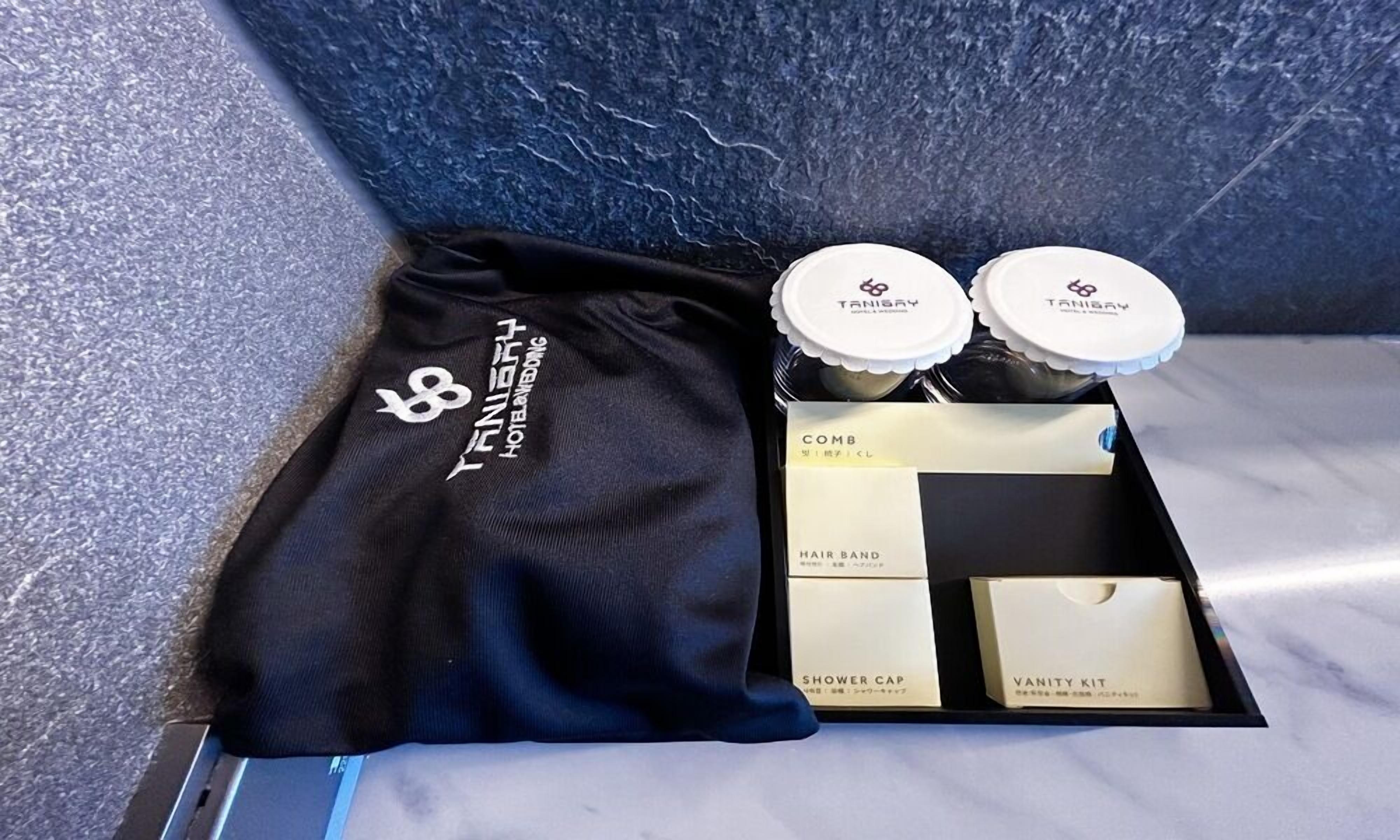 Habitación de hotel con toalla negra, una goma para el pelo, peine, gorro de ducha y kit de tocador.