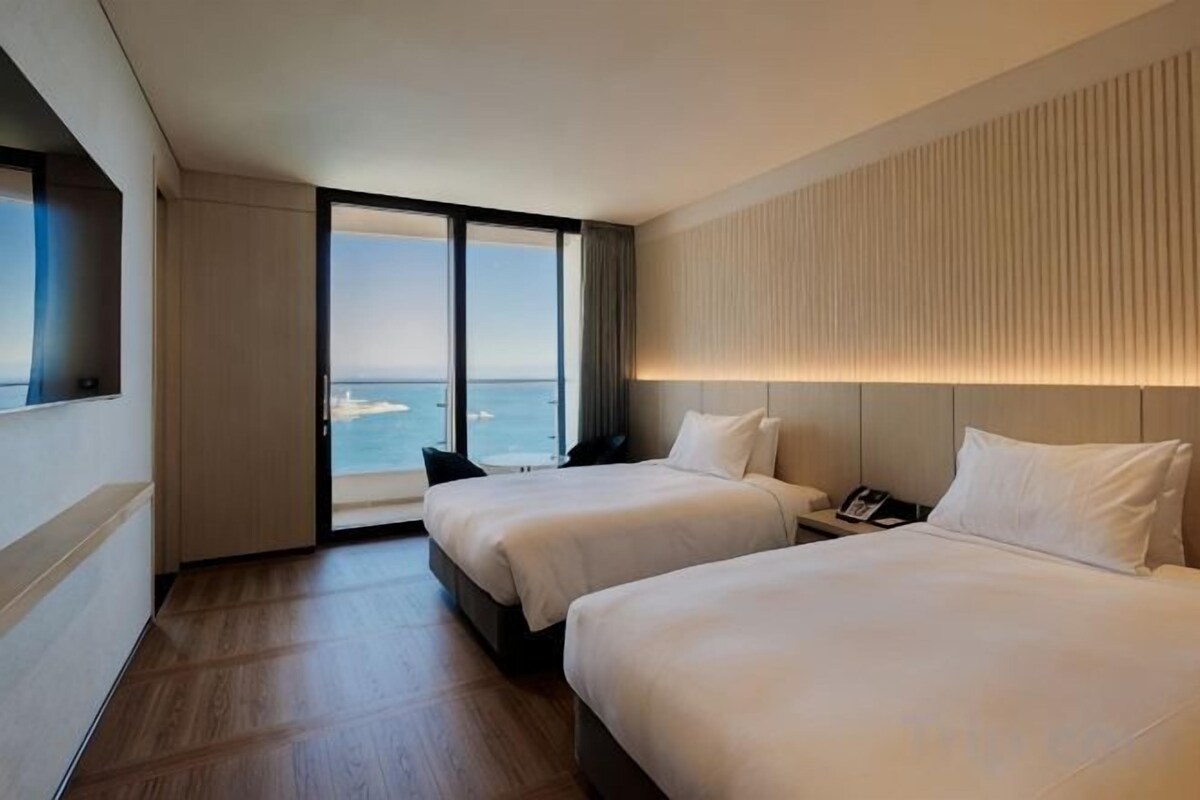 A hotel room with two beds, a large window with a view of the sea, and a modern design.