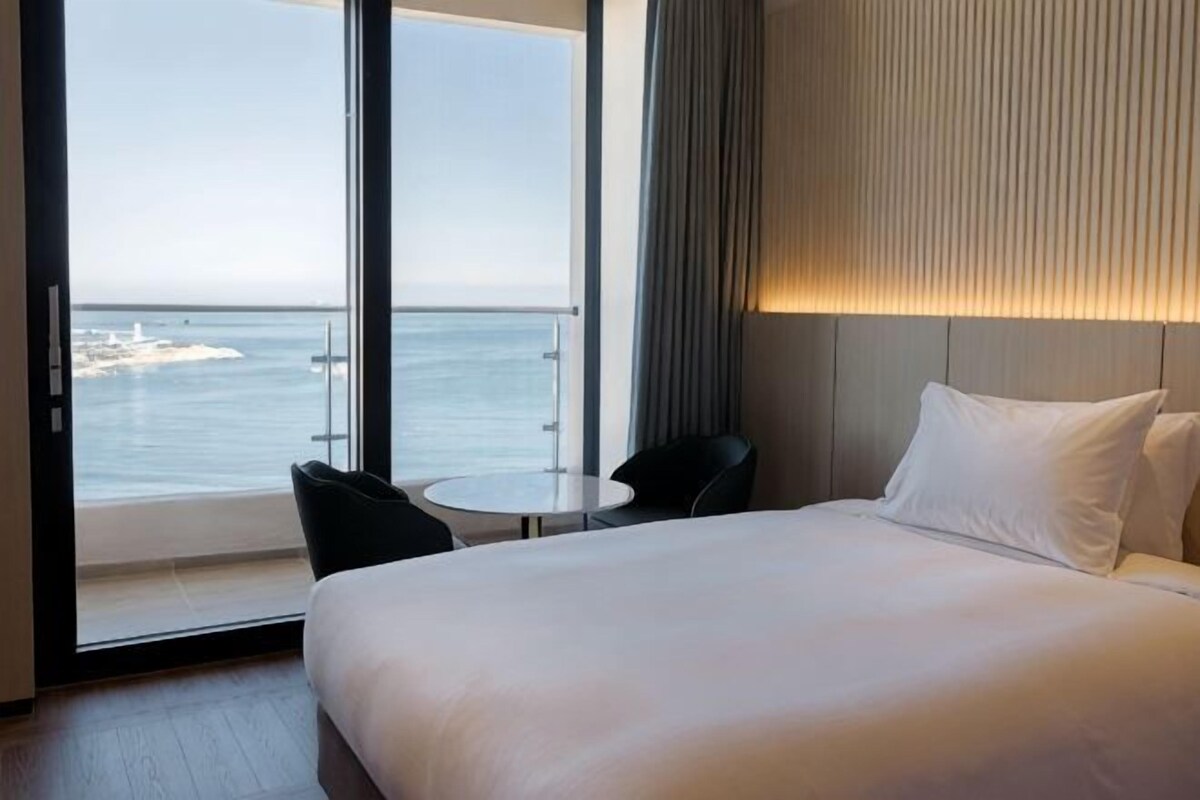 A hotel room with a large bed, a small table, two chairs, and a view of the sea.
