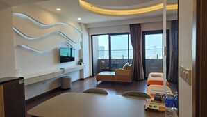 Une chambre d’hôtel moderne dotée d’un coin repas, d’un téléviseur fixé sur un mur ondulé, d’un balcon offrant une vue sur la ville et d’une grande fenêtre avec des rideaux.