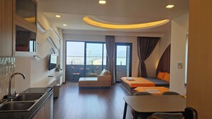 Une chambre d’hôtel moderne dotée d’un coin cuisine, d’une table à manger, d’un canapé et d’un balcon offrant une vue sur la ville.