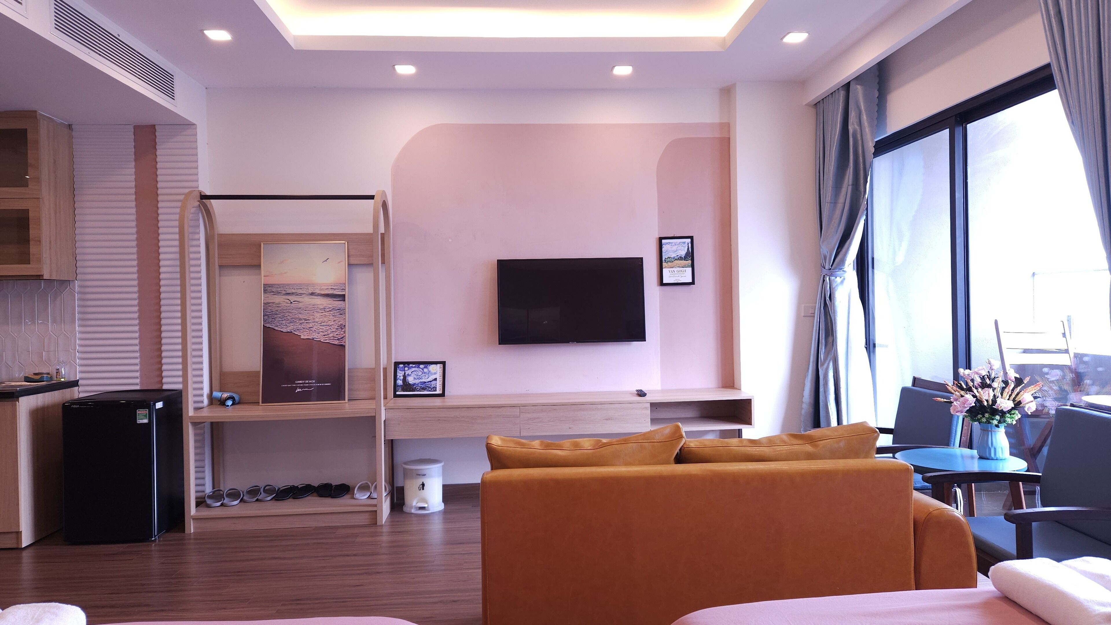 A hotel room with a bed, a TV, a desk with a computer, a small fridge, and a window with curtains.