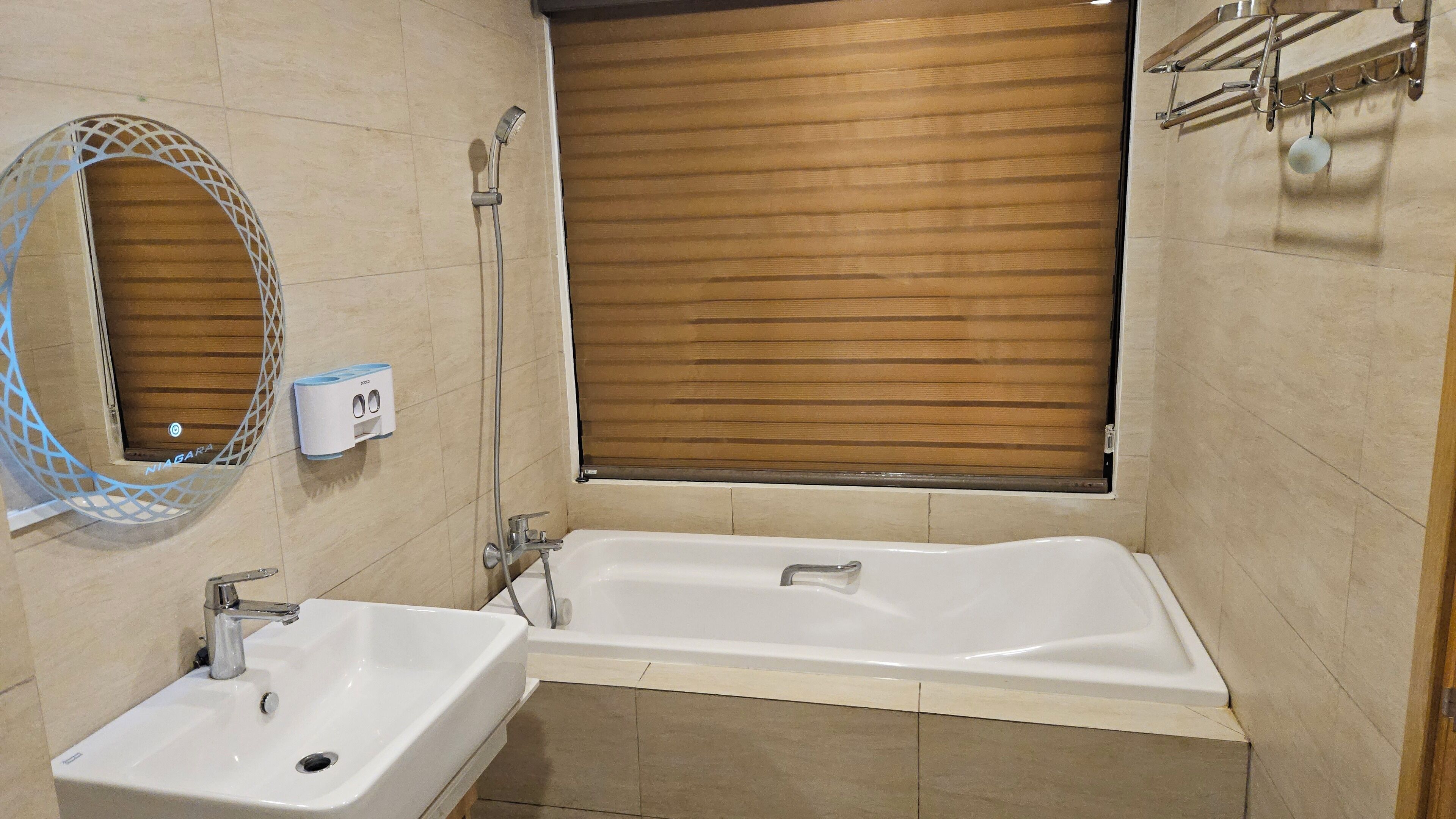 Une salle de bain équipée d’un lavabo, d’une baignoire, d’un store en bois à la fenêtre et d’un porte-serviettes.