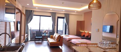 A modern hotel room with a sofa, a dining table with chairs, a TV, and a balcony with a view.