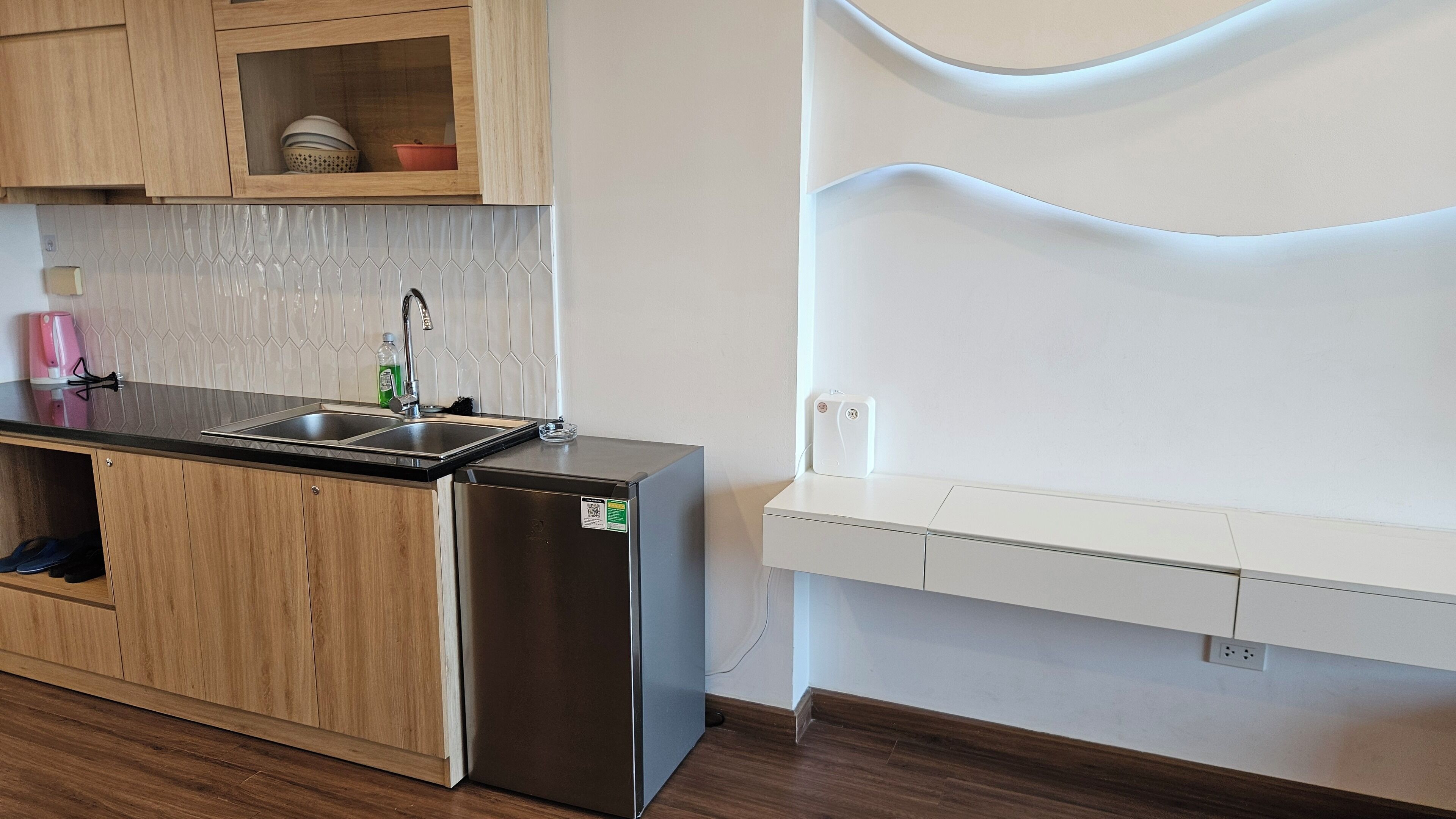 Une cuisine moderne avec des armoires en bois, un réfrigérateur en acier inoxydable, un évier et une étagère blanche intégrée.